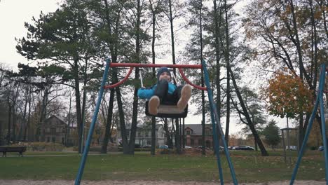 Happy-Boy-is-Swaying-on-Swing-in-Park-at-Autumn-Day-and-Jumping-Out-in-Slow-Motion