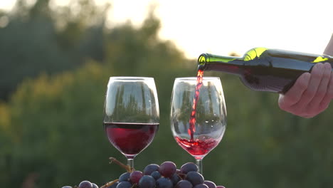 Frauenhand-Gießt-Flasche-Rotwein-In-Weinglas-Bei-Sonnenuntergang-In-Zeitlupe