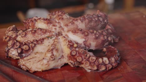 Perfectly-cooked-octopus-placed-on-a-wooden-chopping-board-with-hot-steams-vaporizing-slowly-from-the-delicious-tender-octopus,-handheld-close-up-shot-capturing-details-of-the-suckers-on-each-legs
