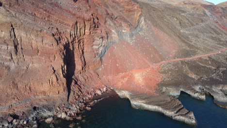 High-rock-formations-and-cliffs-washed-by-the-sea-colored-red,-remnants-of-volcanic-activity,-Cala-Tacoron-,-El-Hierro---circle-drone-shot