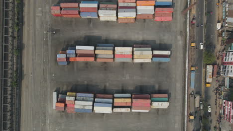 Top-down-aerial-inland-shipping-container-depot-beside-urban-city-road---drone-flight-ascending-shot
