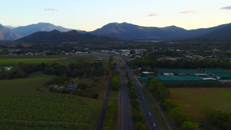 Vehicles-Traveling-On-Scenic-Road-Among-Green-Fields-In-Cairns,-Queensland,-Australia---aerial-drone-shot