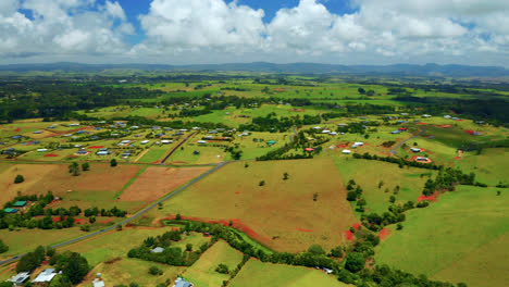Aerial-View-Of-Green-Fields,-Blue-Cloudy-Sky-And-Town-In-Atherton-Tablelands-Region,-Queensland,-Australia---drone-shot