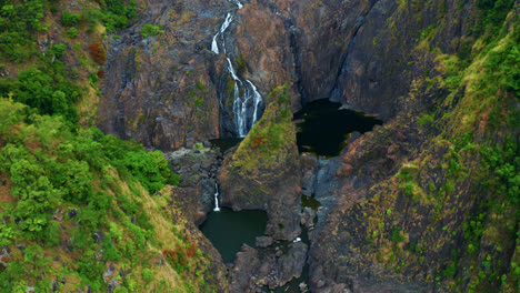 Aerial-View-Of-Waterfall-Cascading-On-Rugged-Cliffs-In-Kuranda,-Queensland,-Australia---drone-shot