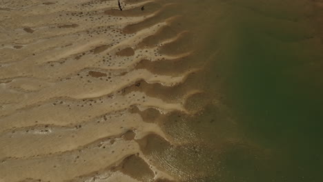 Aerial-top-down-shot-of-sandy-pattern-beside-small-stream-lighting-in-sun---Australia,Queensland