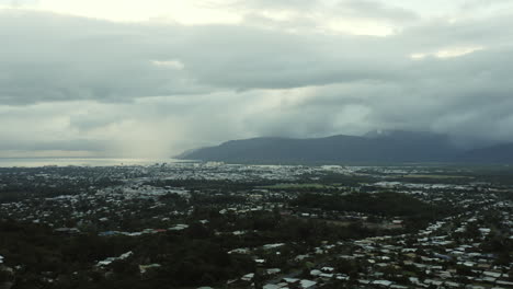Vista-Aérea-De-La-Ciudad-Australiana-Llamada-Cairns-Durante-El-Día-De-Nubes-Densas-Con-Montañas-Y-Océano-En-Segundo-Plano