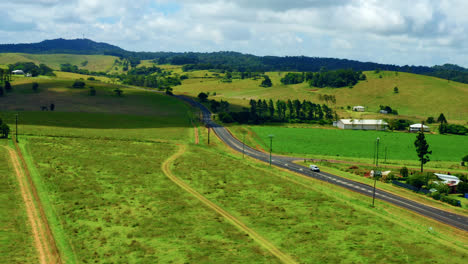 Carretera-Rural-Que-Pasa-Por-Campos-Verdes-En-Las-Mesetas-De-Atherton,-Queensland,-Australia---Toma-Aérea-De-Drones
