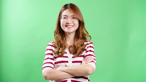 Fröhliche-Junge-Asiatische-Frau-In-Gestreiftem-T-Shirt-Mit-Brille,-Die-In-Die-Kamera-Schaut-Und-Freudig-Lächelnder-Grüner-Bildschirmhintergrund