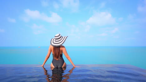 A-healthy,-fit-woman-sits-on-the-edge-of-an-infinity-edge-pool-that-overlooks-the-ocean-horizon