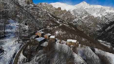 Antenne:-Verschneite-Bergstadt-An-Einem-Berghang-In-Den-Katalanischen-Pyrenäen-Mit-Schneebedeckten-Hohen-Bergen-Im-Hintergrund