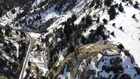 Aerial:-mountainous-terrain-with-a-train-track,-a-river,-some-snow-and-a-viewpoint-with-people