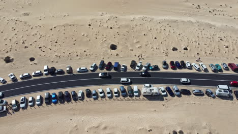 Slow-moving-wandering-cars-along-a-straight-desert-road,-among-parked-cars-near-the-region,-a-clear-and-sunny-day
