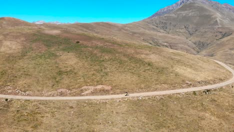 Aerial:-mountain-biker-going-uphill-in-a-high-mountain-deserted-area-in-summer-time-under-a-blue-sky