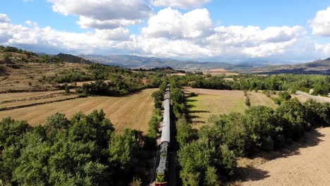 Aerial:-old-diesel-train-traveling-along-fields-under-summer-blue-sky-with-some-clouds-on-a-sunny-day