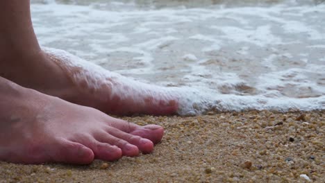 Low-angle-shot-of-a-barefoot-woman-cooling-her-feet-into-the-low-tide-waves-seawater-in-Hong-Kong