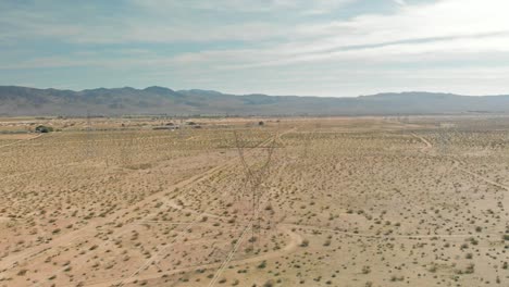 Aerial-view-of-the-Mojave-Desert,-electrical-transmission-towers-and-the-Tehachapi-Mountains-on-an-overcast-day