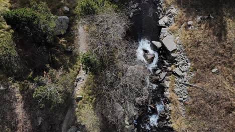 Aerial:-zenital-shot-of-a-river-and-a-path-with-hikers-in-the-mountains
