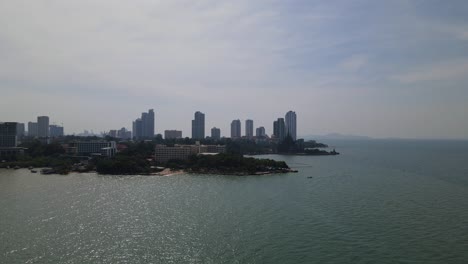 Aerial-descending-footage-of-the-Sanctuary-of-Truth-in-Pattaya-with-the-city-buildings-in-the-background,-Chonburi,-Thailand