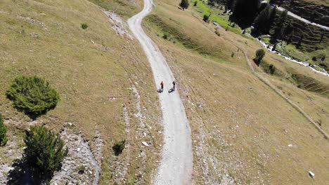 Aerial:-two-mountain-bikers-going-downhill-in-a-high-mountain-in-summer-time