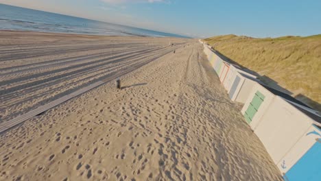 FPV-drone-shot-of-grassy-dunes-and-an-empty-beach-during-a-summer-sunset