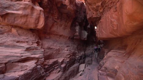 Man-Walking-into-Slot-Canyon-Between-Steep-Sandstone-Cliffs-in-Desert,-Wadi-Rum,-Jordan,-Tilt-Down-Revealing-Wide-View