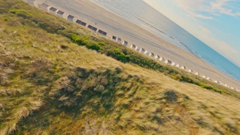 FPV-drone-shot-flying-at-high-speed-over-an-empty-beach-and-grassy-green-dunes-during-sunset