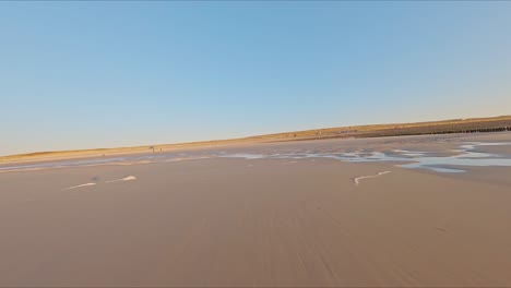 Wunderschöne-Hochgeschwindigkeits-FPV-Drohne,-Die-Während-Eines-Wolkenlosen-Sonnenuntergangs-über-Die-Brandung-Eines-Strandes-Fliegt
