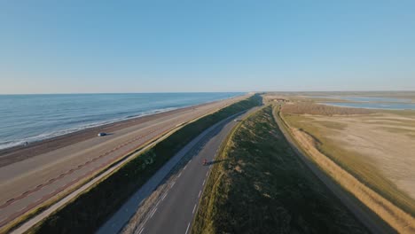 Aerial-tracking-shot-of-a-motorcyclist-on-an-asphalt-coastal-road-on-a-dike-along-a-blue-sea-on-a-beautiful-sunny-day