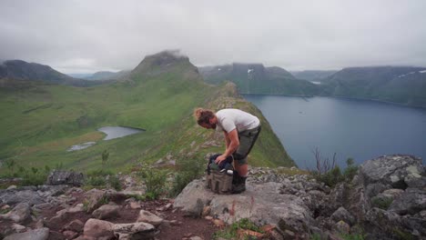 Hiker-Putting-Clothes-On-His-Bacpack-With-Segla-Mountains-At-Background-In-Senja-Island,-Northern-Norway