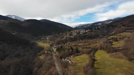 Luftaufnahme:-Annäherung-An-Eine-Kleine-Bergstadt-In-Einer-Bergigen-Landschaft-Mit-Schneebedeckten-Bergen-Im-Hintergrund