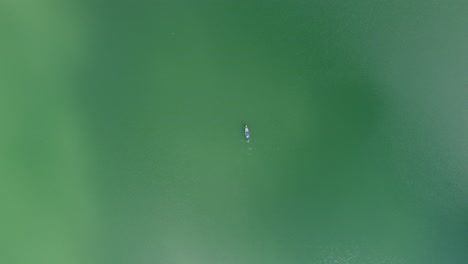 Vista-Aérea-De-Personas-Remando-Un-Bote-De-Madera-En-Un-Lago-O-Mar-Azul-Turquesa