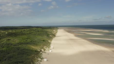 Aerial-shot-of-lush-green-dunes-and-a-beautiful-white-beach-where-sand-gets-swept-away-by-the-wind
