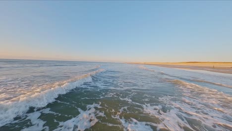 Spectacular-FPV-drone-shot-flying-closely-over-breaking-waves-at-high-speed-during-sunset-on-a-cloudless-day