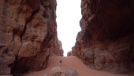 Back-View-of-Lonely-Man-Walking-on-Sand-in-Canyon-Under-Steep-Sandstone-Cliffs