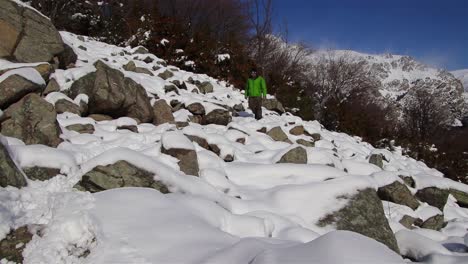 Hombre-Vestido-Con-Un-Anorak-Verde-Caminando-Por-Un-Sendero-De-Montaña-Entre-Rocas