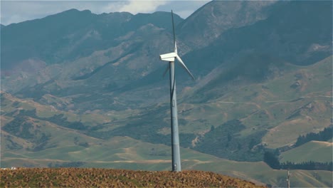 Drehende-Windmühle-Mit-Bergen-Im-Hintergrund,-Windenergie-Windkraftanlage-Zur-Stromerzeugung,-Grüne-Energiezukunft---Stetiger-Schuss