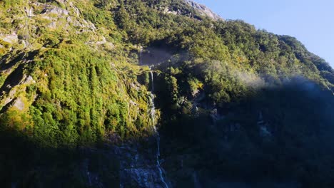 Tilt-down-shot-of-tropical-waterfall-falling-down-the-vegetated-mountain-lighting-in-sun