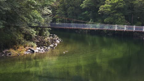 Panning-shot-of-tropical-river-and-wooden-chain-bridge-connecting-jungle-and-rainforest