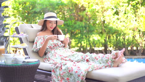 A-pretty-young-woman-relaxing-on-a-sun-lounger-poolside-selects-her-coffee-cup-from-the-resort-coffee-service