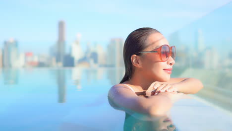 Close-up-of-a-woman's-head-and-shoulders-while-she-leans-along-the-edge-of-a-rooftop-swimming-pool