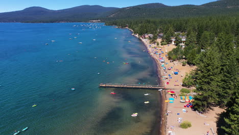 Aerial-landscape-view-of-people-relaxing-on-a-sandy-lake-beach-surrounded-by-a-pine-forest-in-Lake-Tahoe