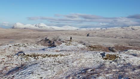 Parallaxe-Luftaufnahme-Eines-Mannes,-Der-Auf-Dem-Schneebedeckten-Hügel-Von-Ullapool-In-Schottland-Steht