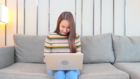 A-young-woman-sitting-on-a-couch-works-on-her-laptop-with-sucess