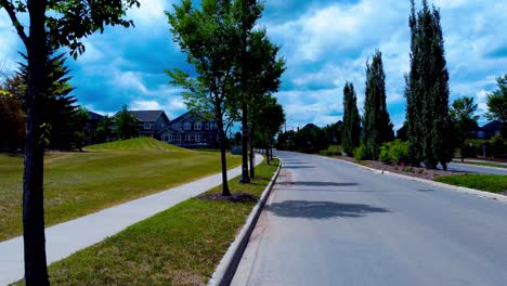 Summer-blue-white-clouds-forming-at-mysterious-driveway-leading-to-some-massive-luxury-homes-on-a-windy-bright-afternoon-with-rows-of-tall-lush-green-trees-revealing-optical-zoom-into-entrance-path
