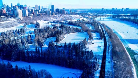 aerial-dolly-roll-over-the-winter-snow-cover-river-valley-Victoria-park-with-the-newly-made-skating-rink-oval-outdoor-with-a-speed-skating-race-track-with-the-city-of-Edmonton-in-the-background-sunny