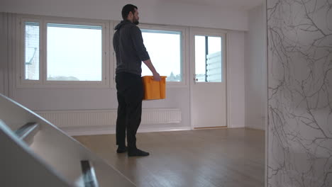 Man-walks-through-empty-new-house-and-picks-up-a-box-to-unpack