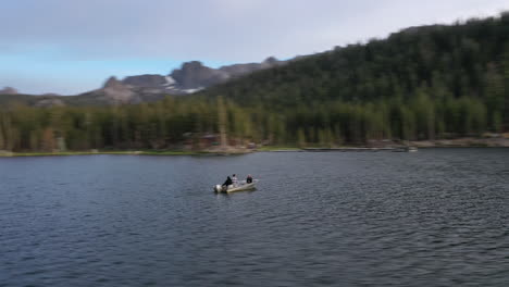 Aerial-view-spinning-around-a-boat-on-a-mountain-lake-surrounded-by-a-pine-forest-in-Mammoth-Lakes,-CA