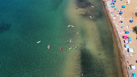 Aerial-top-view-of-people-relaxing-on-a-sandy-beach-next-to-crystal-clear-water-in-Lake-Tahoe