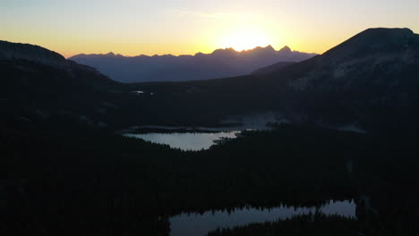 Aerial-landscape-view-of-a-mountain-lake-surrounded-by-a-pine-trees-forest,-at-dusk-in-Mammoth-Lakes,-CA