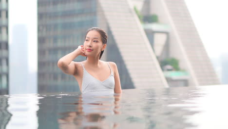 A-woman-in-a-rooftop-swimming-pool-reaches-up-to-brush-her-hair-away-from-her-face